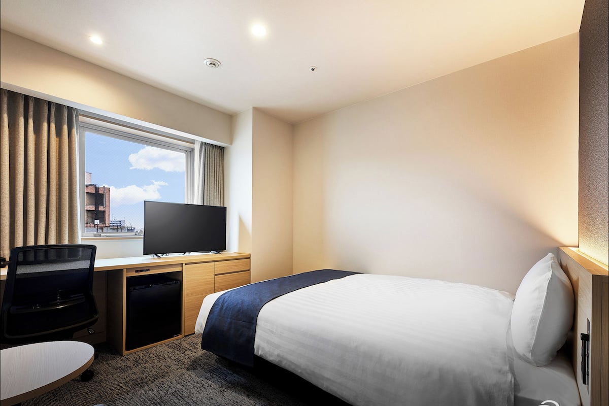 Een hotelkamer met een bed, een bureau met een computer, een televisie en een raam met gordijnen.