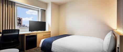 Habitación de hotel con cama, escritorio con computadora, televisor y ventana con cortinas.
