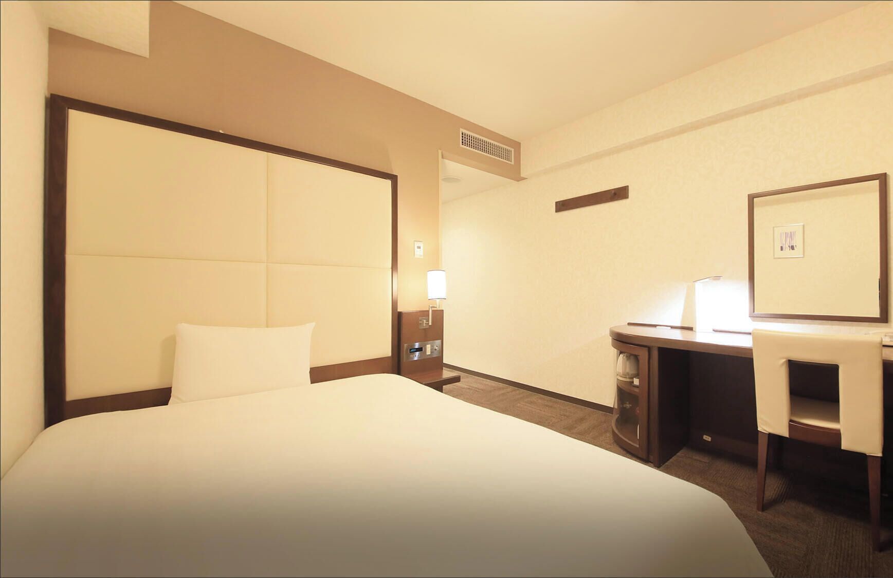A hotel room with a large bed, a desk, a chair, a lamp, and a mirror.