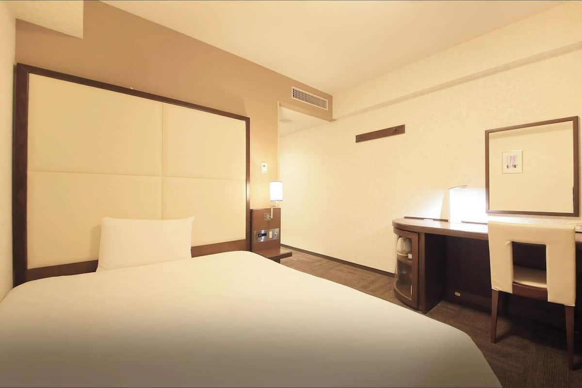 Une chambre d’hôtel avec un grand lit, un bureau, une chaise, une lampe et un miroir.