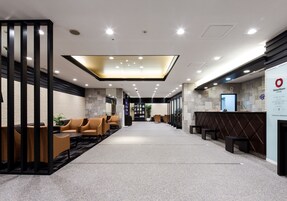 Un moderno vestíbulo de hotel con mostrador de recepción, zona de estar y un llamativo elemento decorativo iluminado en el techo.