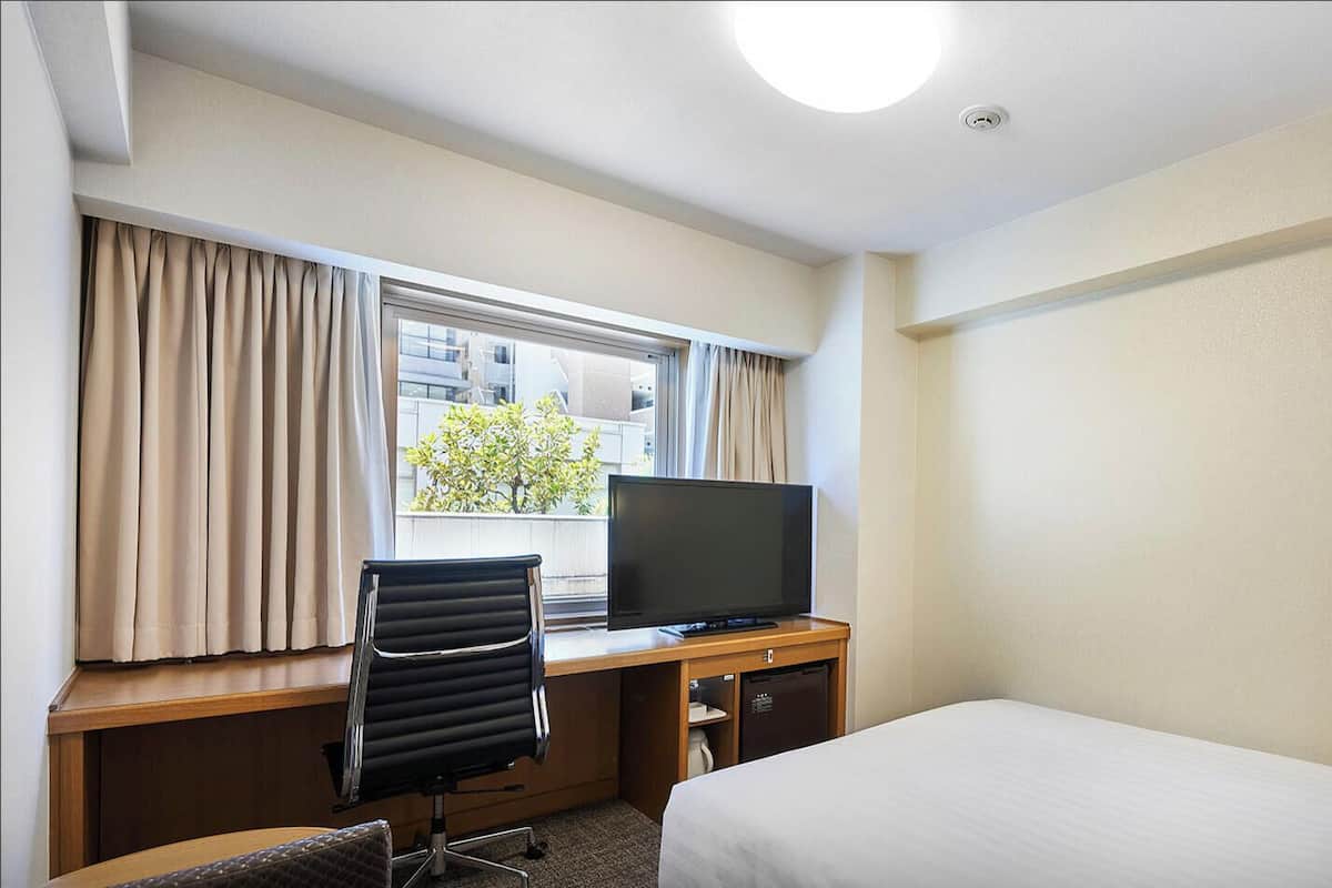 Une chambre d’hôtel comprenant un lit, un bureau avec une télévision, une chaise et une lampe.
