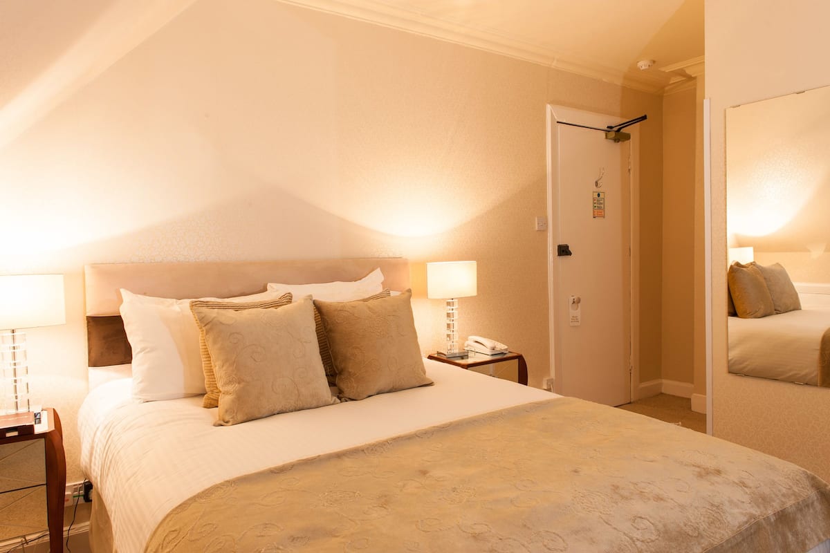 A hotel room with a bed, bedside lamp, and a door with a mirror.