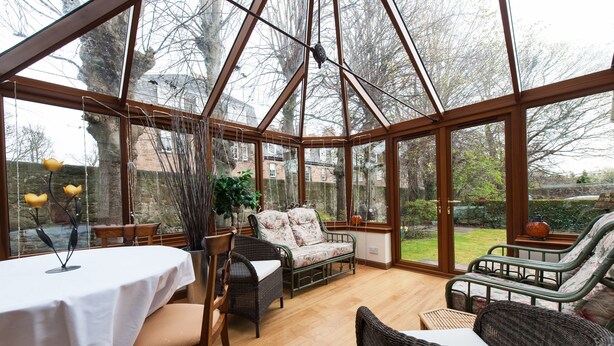 A conservatory with a table and chairs, a sofa, and a view of the garden. - Kildonan Lodge Hotel (Edinburgh)
