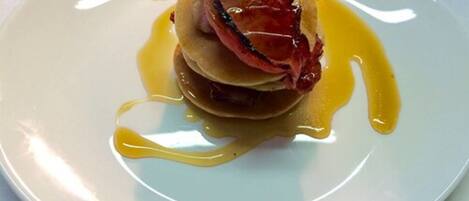 A plate with pancakes, bacon, and a sauce.