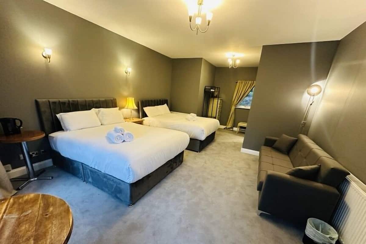 A hotel room with two beds, a sofa, a small table, and a radiator.
