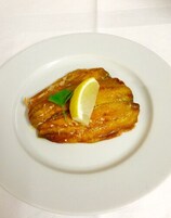 A white plate with a single piece of food garnished with a lemon slice and a sprig of parsley.