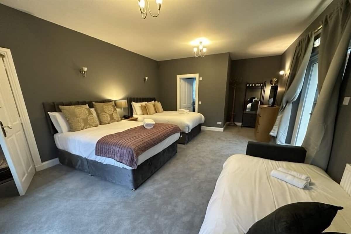 A hotel room with two large beds, a sitting area, a wardrobe, and a mirror.