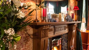 A grand room with a fireplace, ornate wooden mantel, and red lamps. - Kildonan Lodge Hotel (Edinburgh)