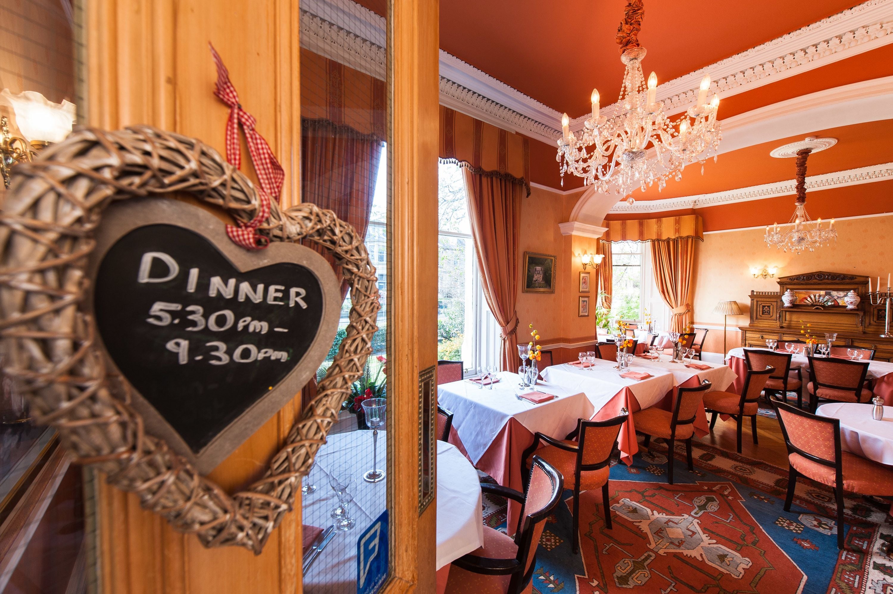 A restaurant interior with tables set for dining, a chandelier, and a chalkboard sign indicating dinner hours.