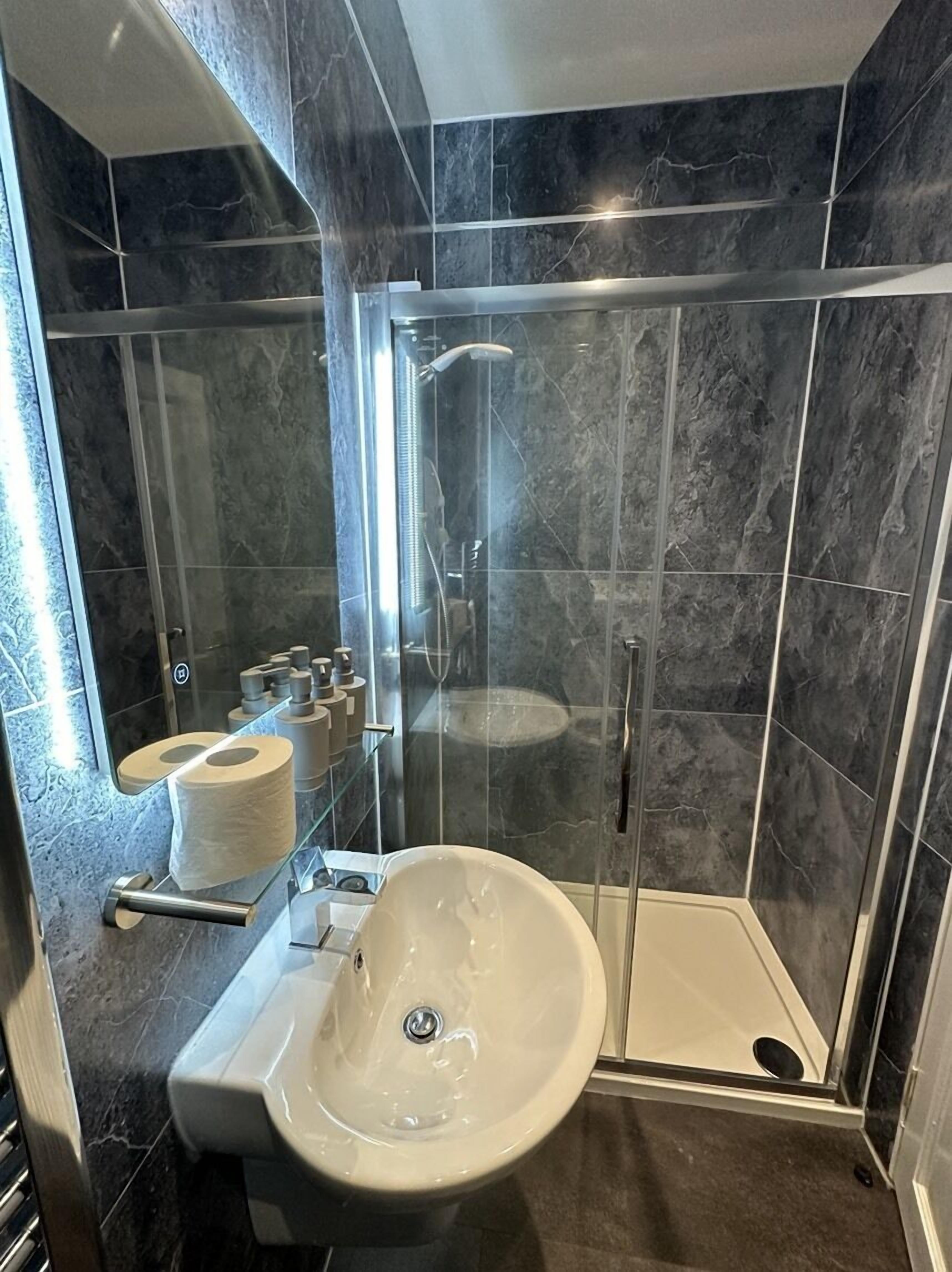 A modern bathroom with a glass-enclosed shower, a pedestal sink, and marble walls.