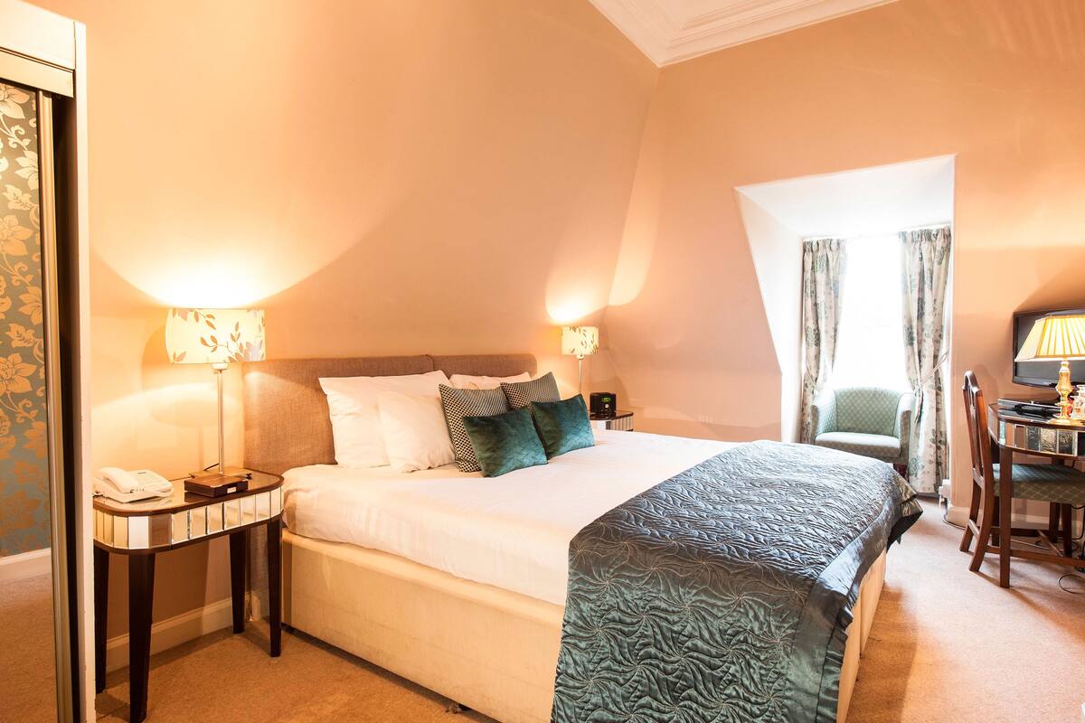 A hotel room with a large bed, two bedside lamps, a desk with a chair, and a television.