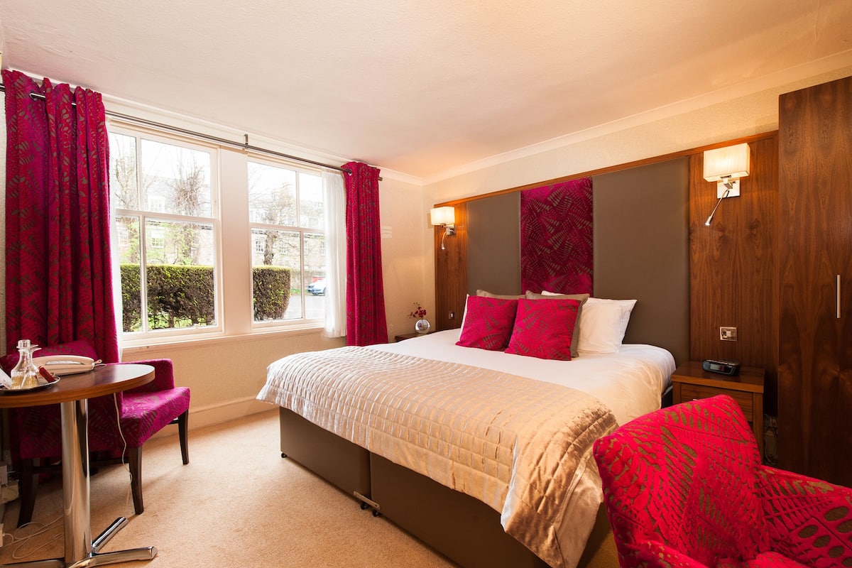 A bedroom with a bed, a desk, a chair, a wardrobe, and a window with curtains.