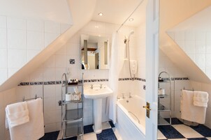 A bathroom with a white sink, a bathtub, and a shower. There are two towel racks with towels hanging on them. The floor is tiled with a blue and white pattern.