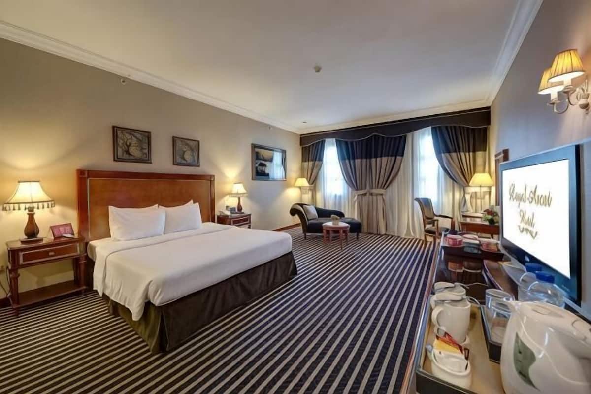 Une chambre d’hôtel avec un grand lit, deux tables de chevet avec des lampes, un bureau avec une chaise, une télévision et une fenêtre avec des rideaux.