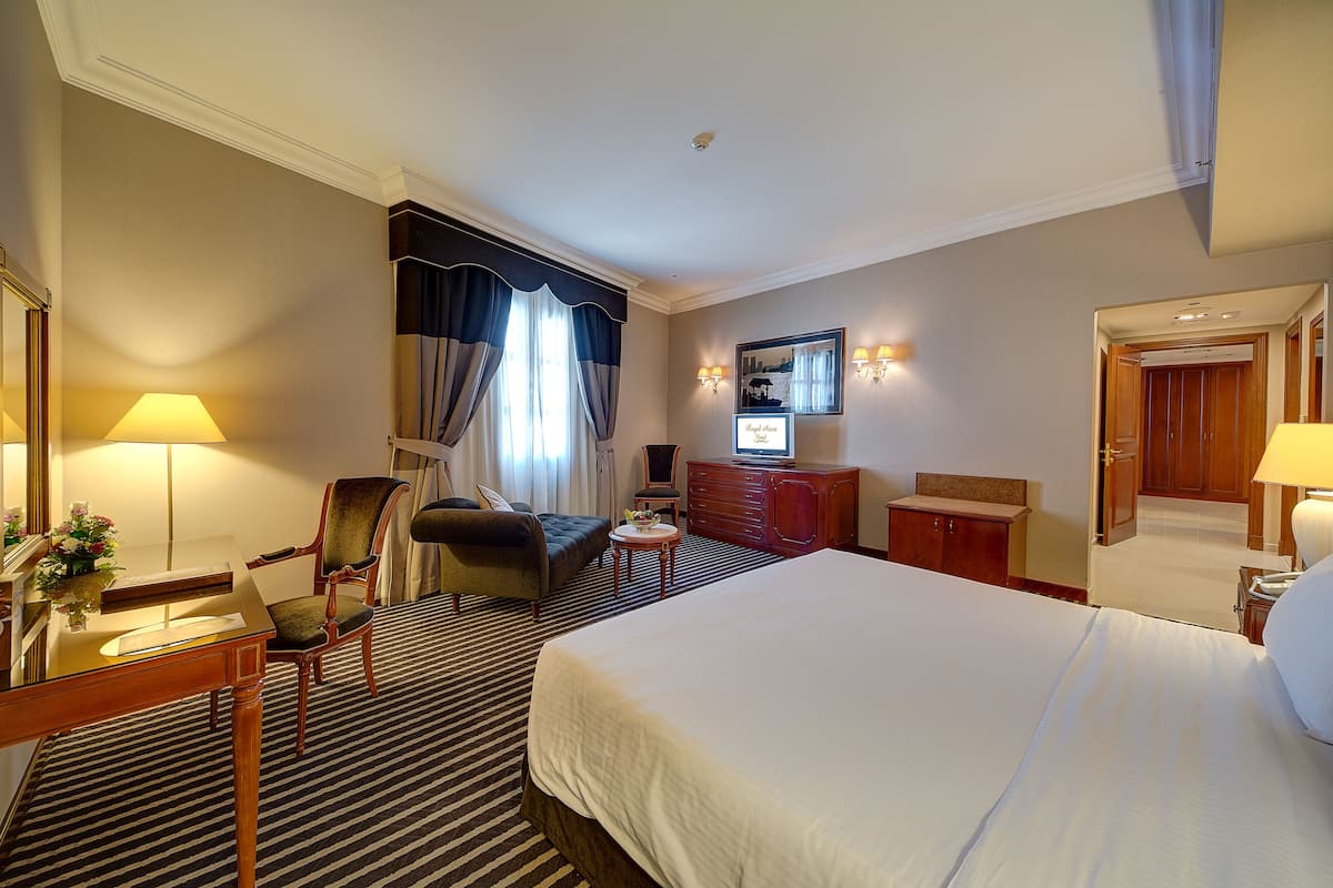 Une chambre d’hôtel avec un grand lit, un bureau avec une lampe, une chaise, une commode et un téléviseur.
