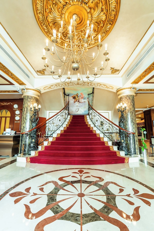 A grand staircase with a red carpet, a chandelier, and ornate columns.