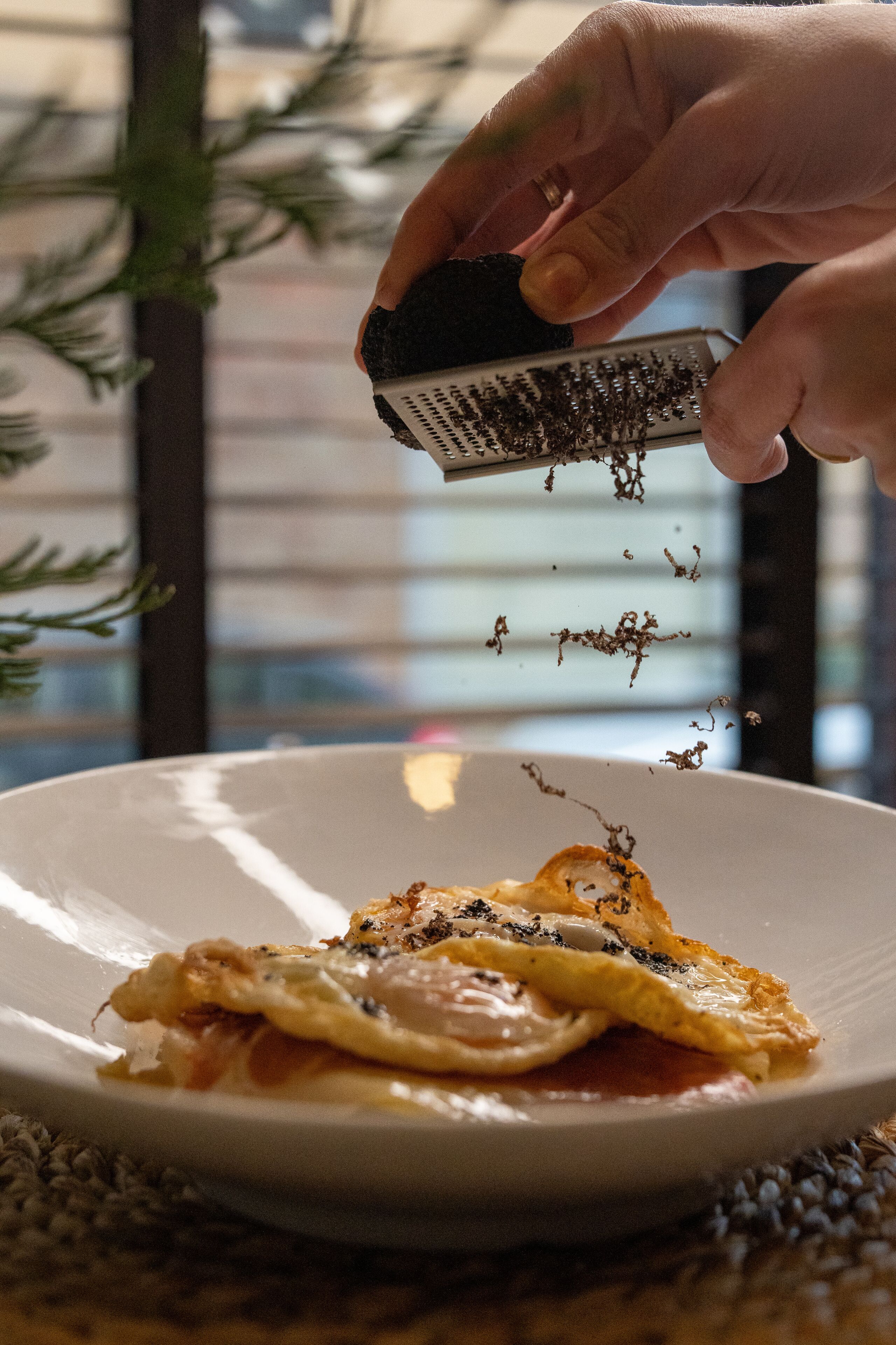 A hand grating cheese over a dish with eggs and ham.