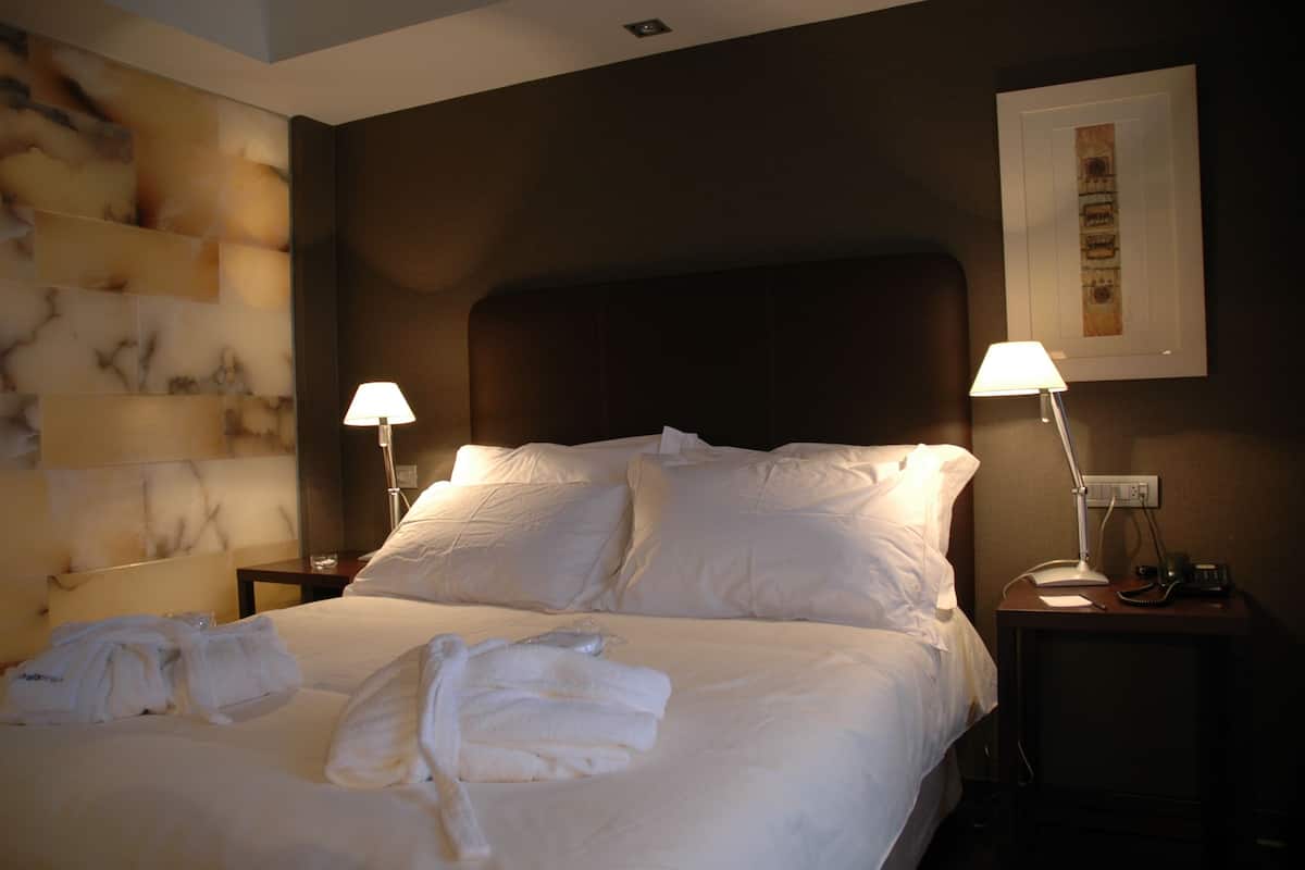 A neatly made bed with white linens, two bedside lamps, and a framed picture on the wall.