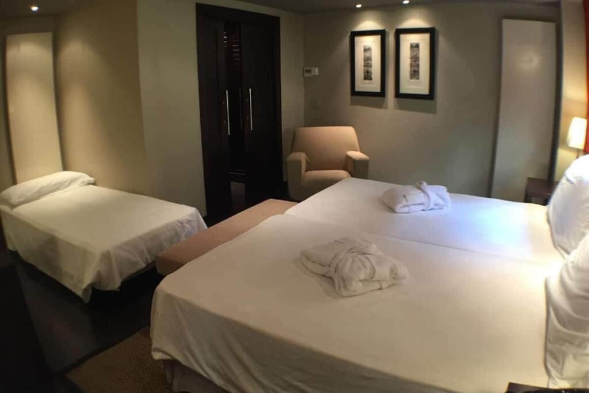 A hotel room with two single beds, a sofa, a chair, and a wardrobe.