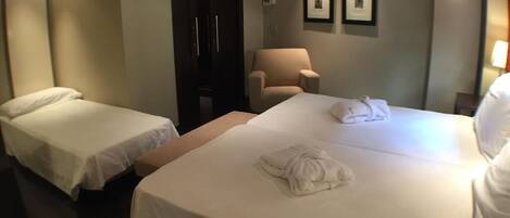 Una habitación de hotel con dos camas individuales, un sofá, una silla y un armario.