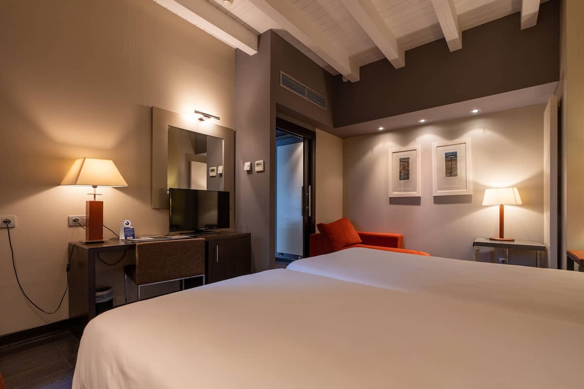 A hotel room with a large bed, a desk with a lamp, a television, and a door leading to another room.