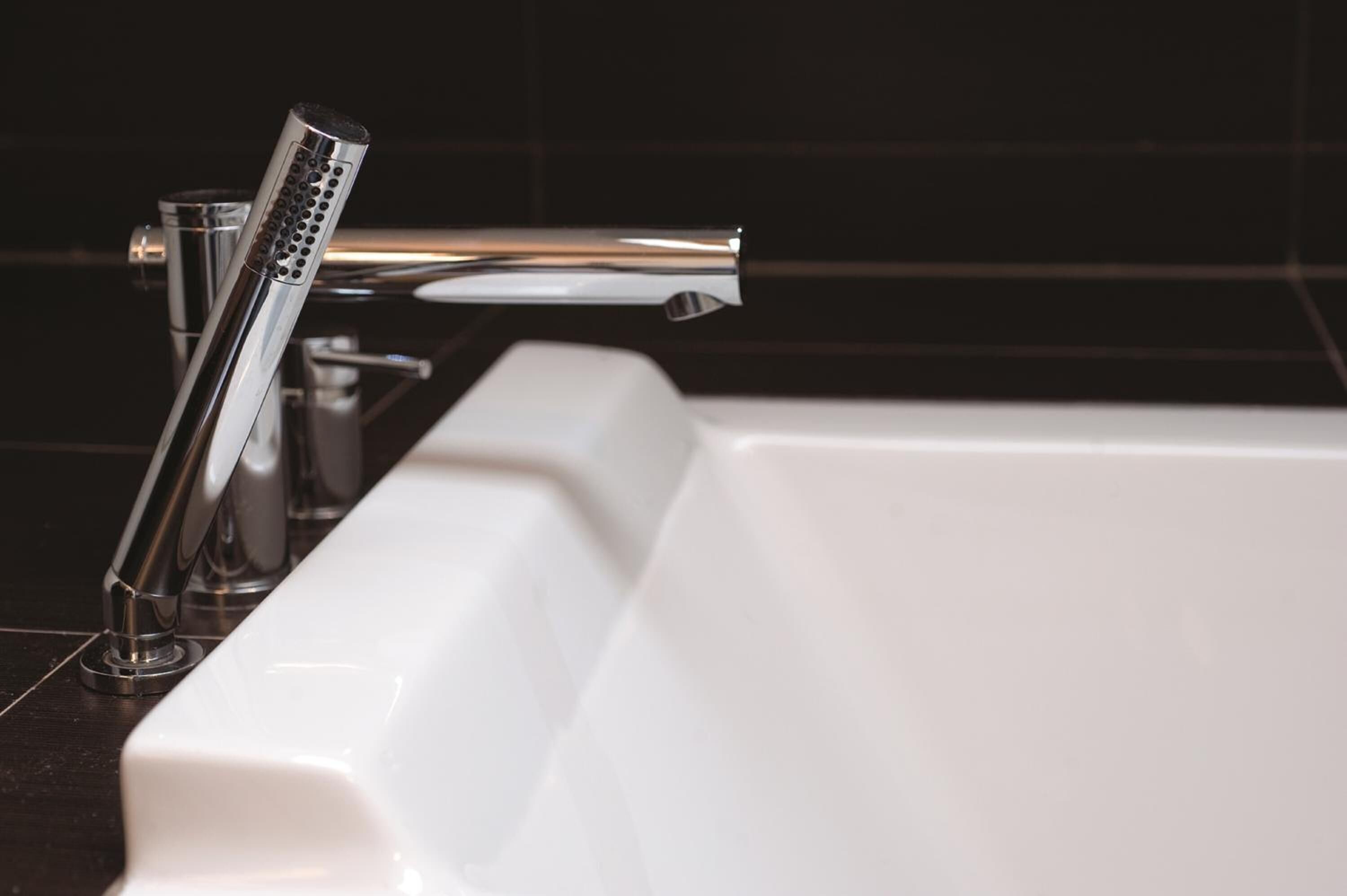 A modern bathroom with a chrome faucet, a glass soap dispenser, and a white bathtub.