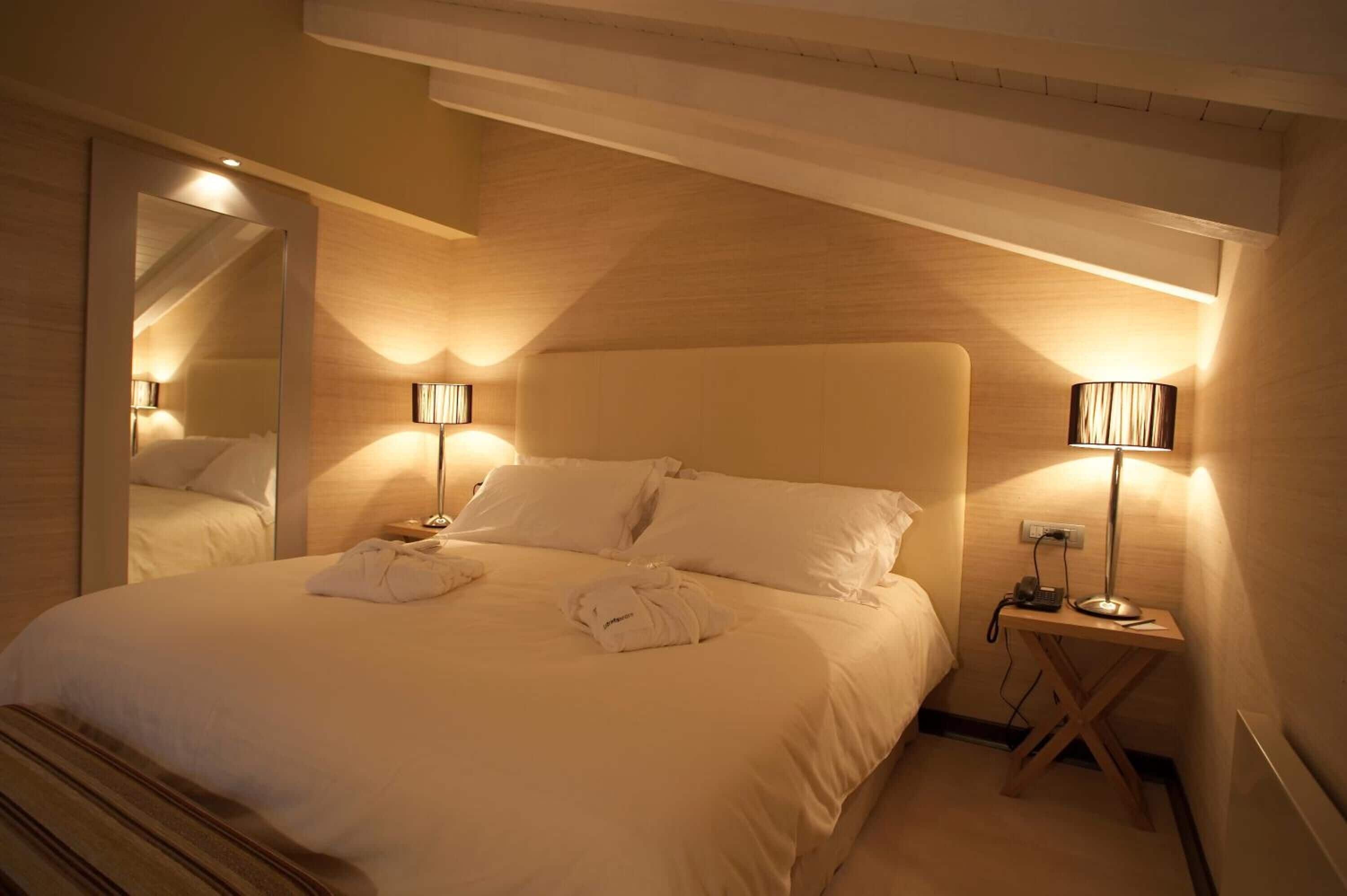 Habitación de hotel con una cama grande, dos lámparas de noche, un espejo y techo de madera.