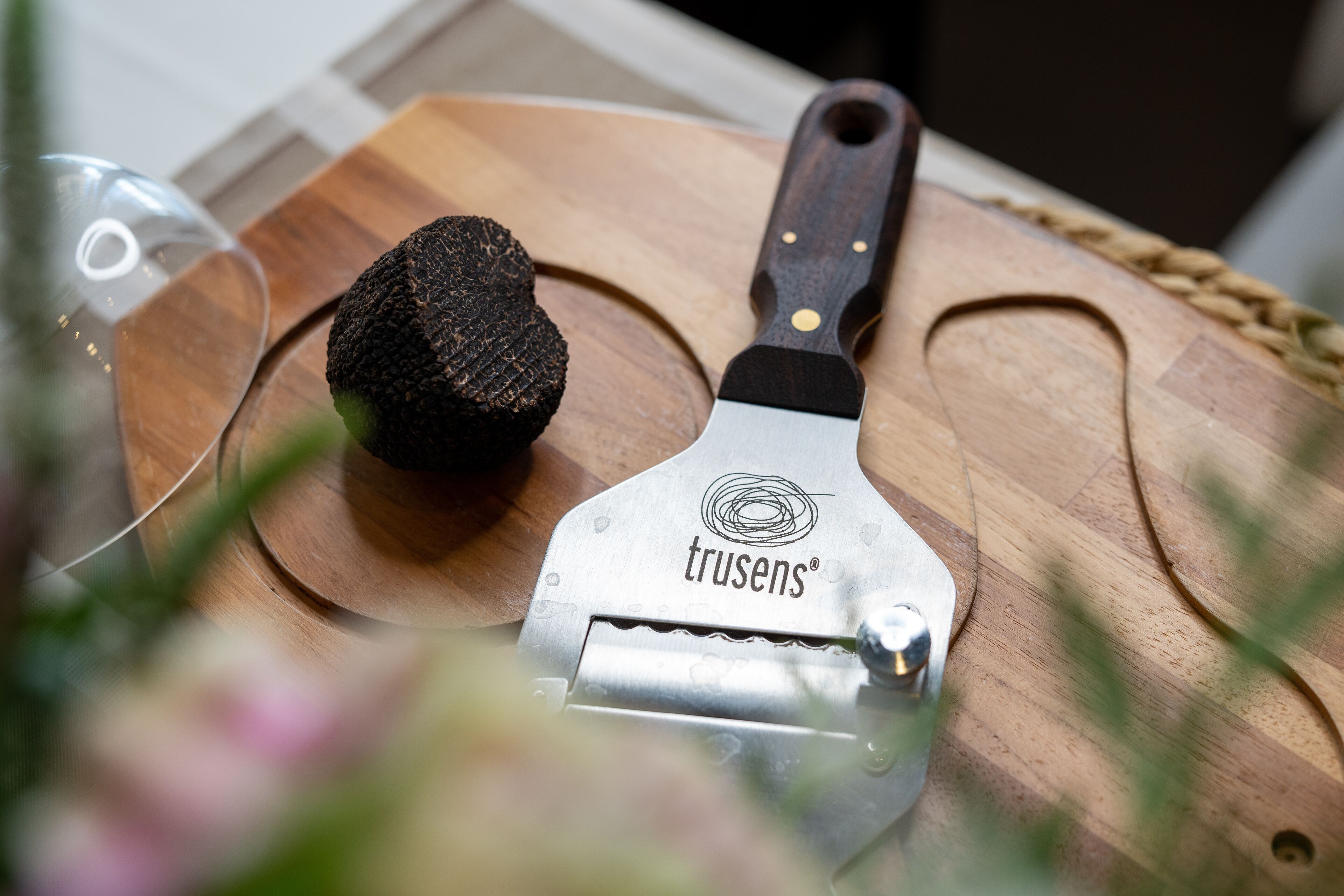 A kitchen utensil with a wooden handle and a metal blade, resting on a wooden cutting board.