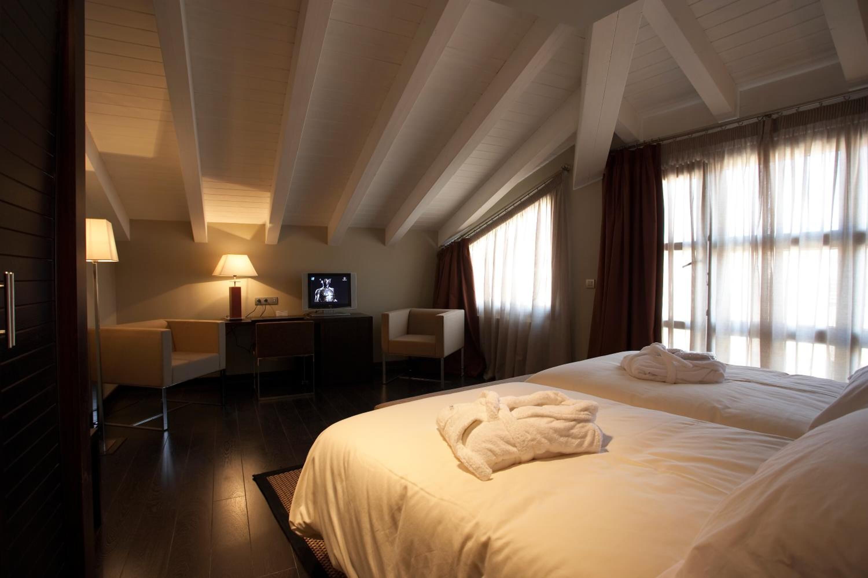 A hotel room with two beds, a desk, a chair, a television, and a window with curtains.