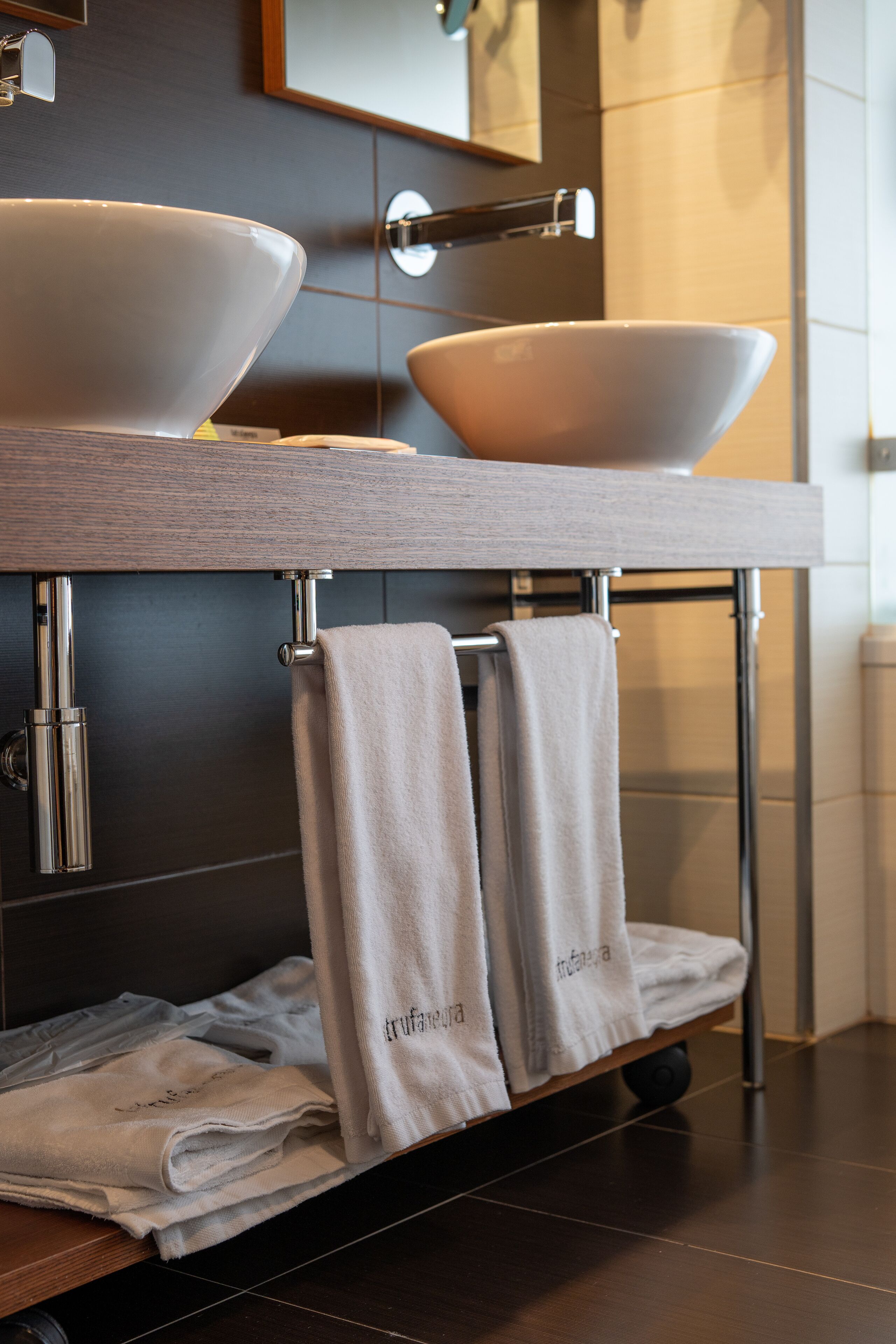 A bathroom with two large white sinks, a towel rack with folded towels, and a mirror above the sinks.