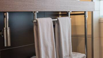 A bathroom with two large white sinks, a towel rack with folded towels, and a mirror above the sinks.