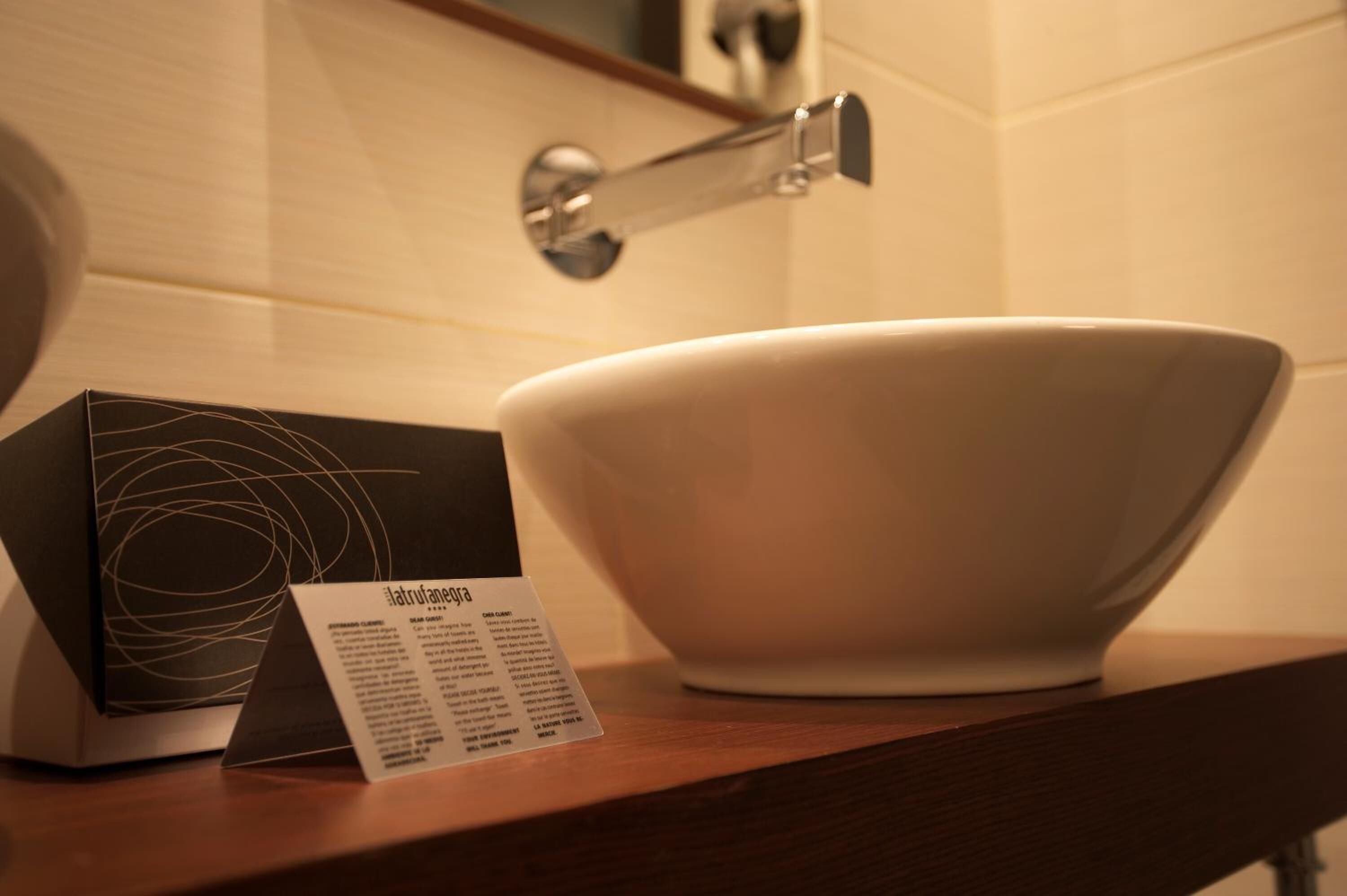 Un bol en céramique blanche posé sur un comptoir en bois, une boîte noire ornée d’un motif blanc et une petite carte d’information.