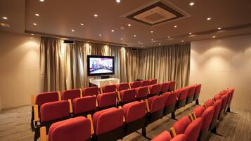 A conference room with rows of red chairs, a large screen, and curtains.