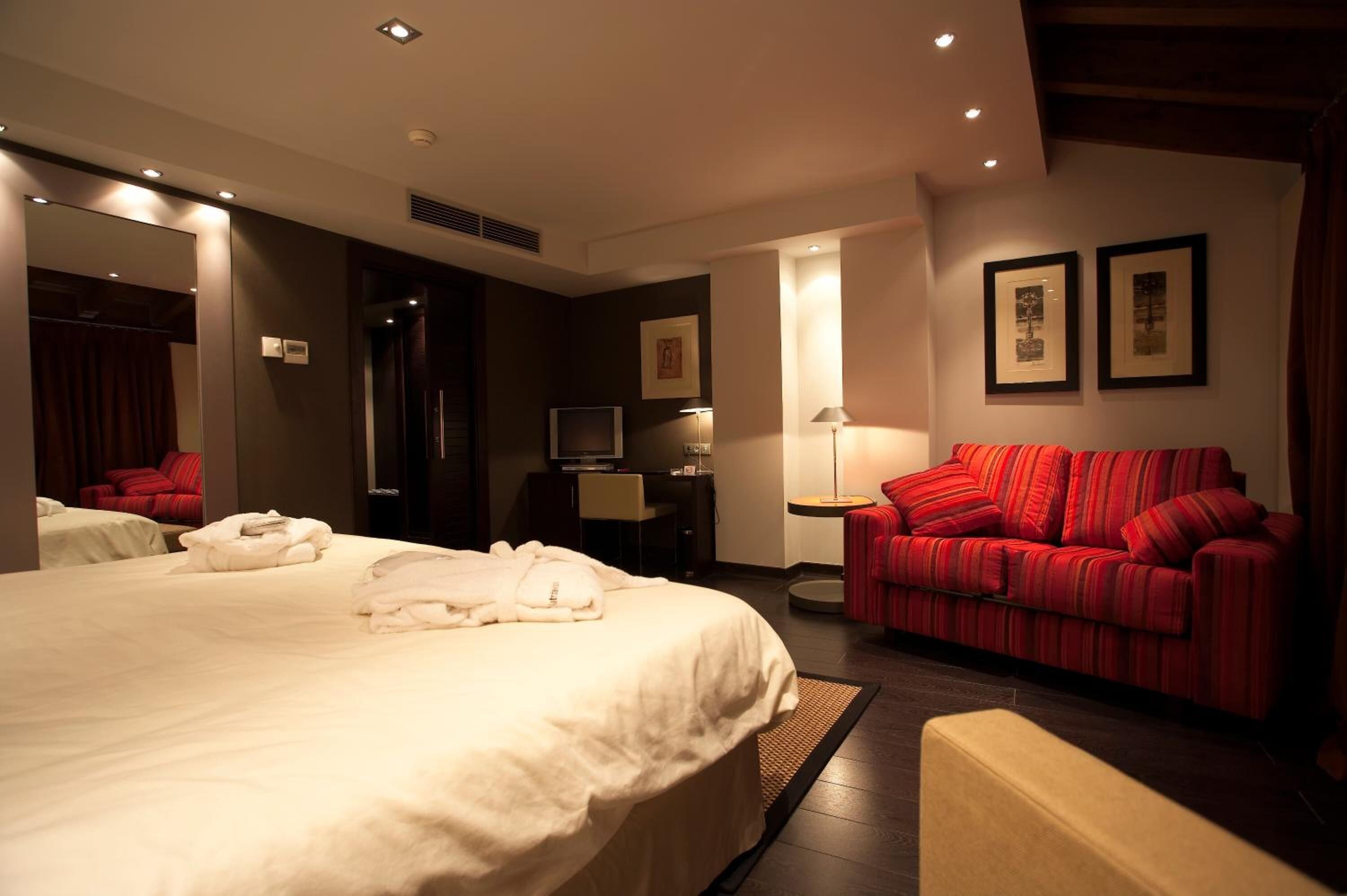Habitación de hotel con una cama grande, un sofá rojo, un televisor y cuadros en la pared.
