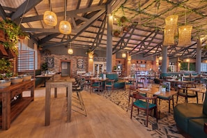 Un restaurant spacieux avec de hauts plafonds, des luminaires suspendus en osier et différents types de sièges, notamment des tables et des banquettes.