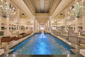 Une grande piscine intérieure dotée d’une fontaine, entourée d’espaces aménagés pour s’asseoir et de colonnes.