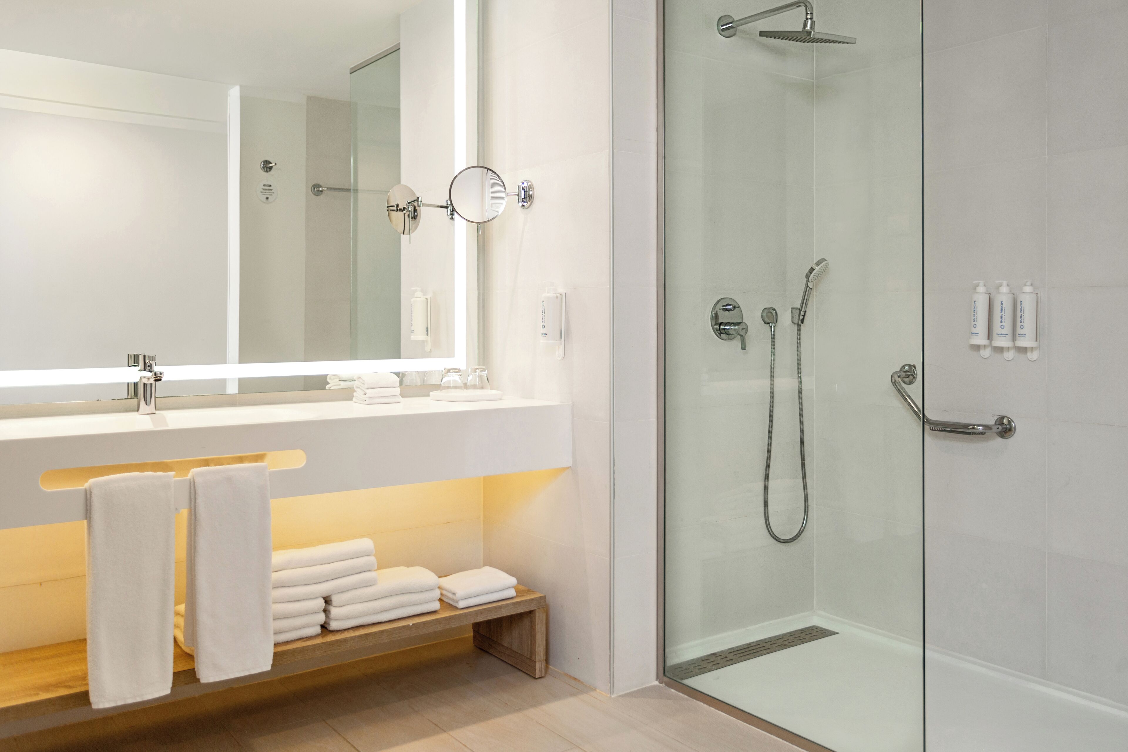 Un baño moderno con cabina de ducha de vidrio, un espejo grande y tocador con perchero.