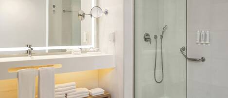 Un baño moderno con cabina de ducha de vidrio, un espejo grande y tocador con perchero.