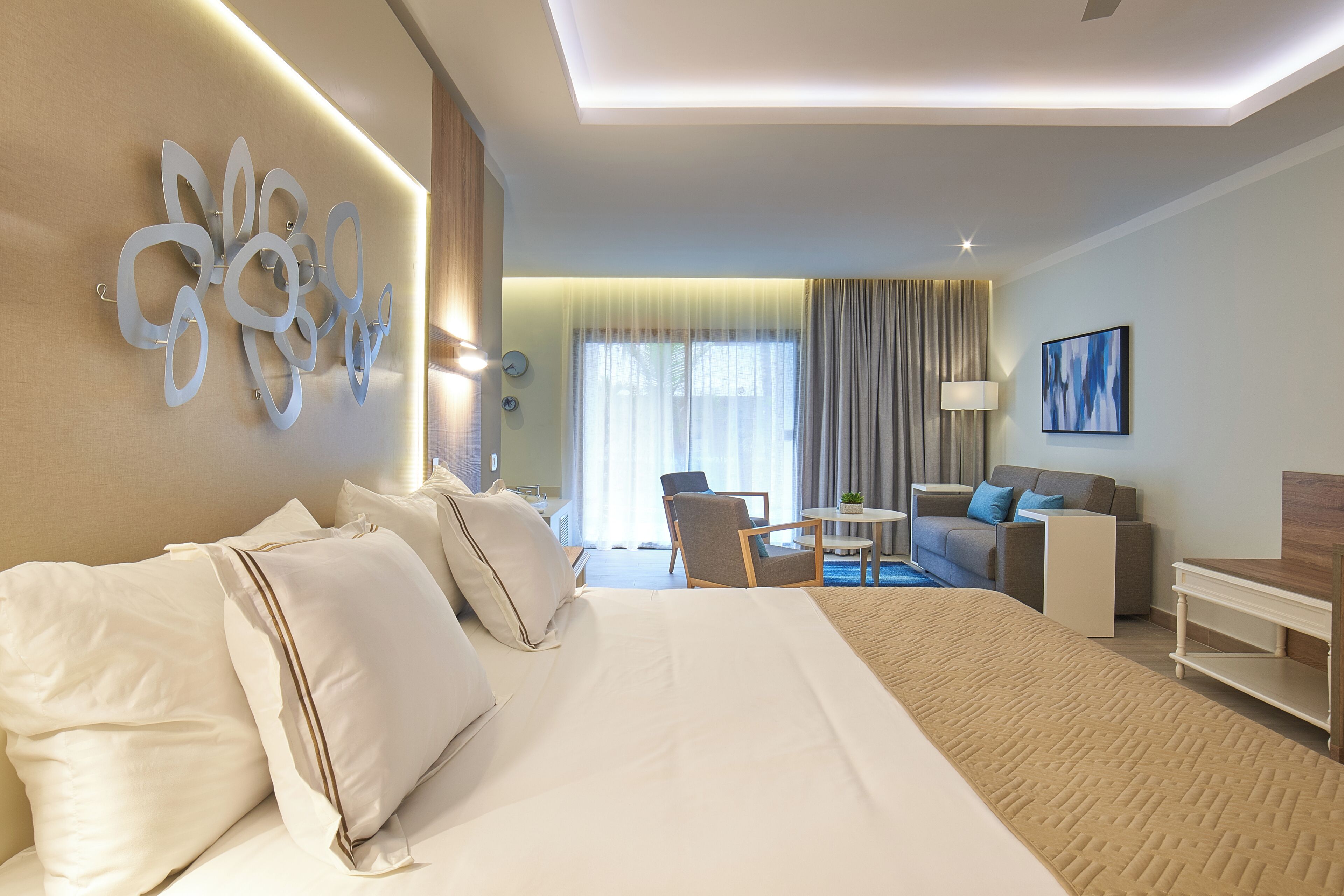 A hotel room with a large bed, a seating area with a sofa and armchairs, a small table, and a painting on the wall.