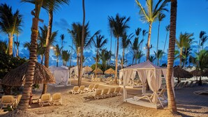 Un complexe hôtelier de bord de mer avec des bungalows aux toits de chaume, des chaises longues et des palmiers.