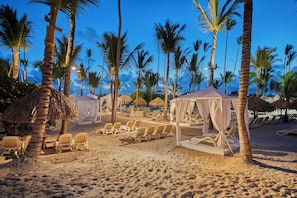 Un complexe hôtelier de bord de mer avec des bungalows aux toits de chaume, des chaises longues et des palmiers.