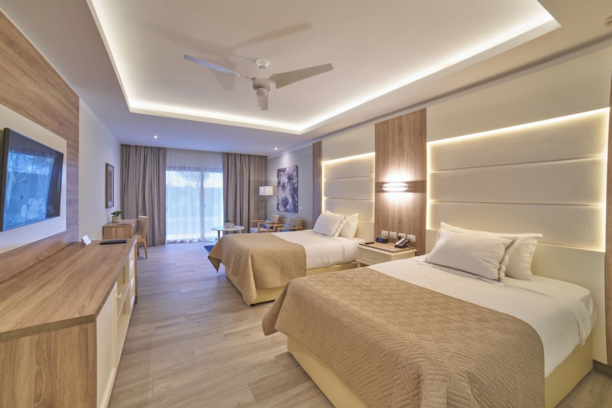 A hotel room with two beds, a desk, a ceiling fan, and a TV on the wall.