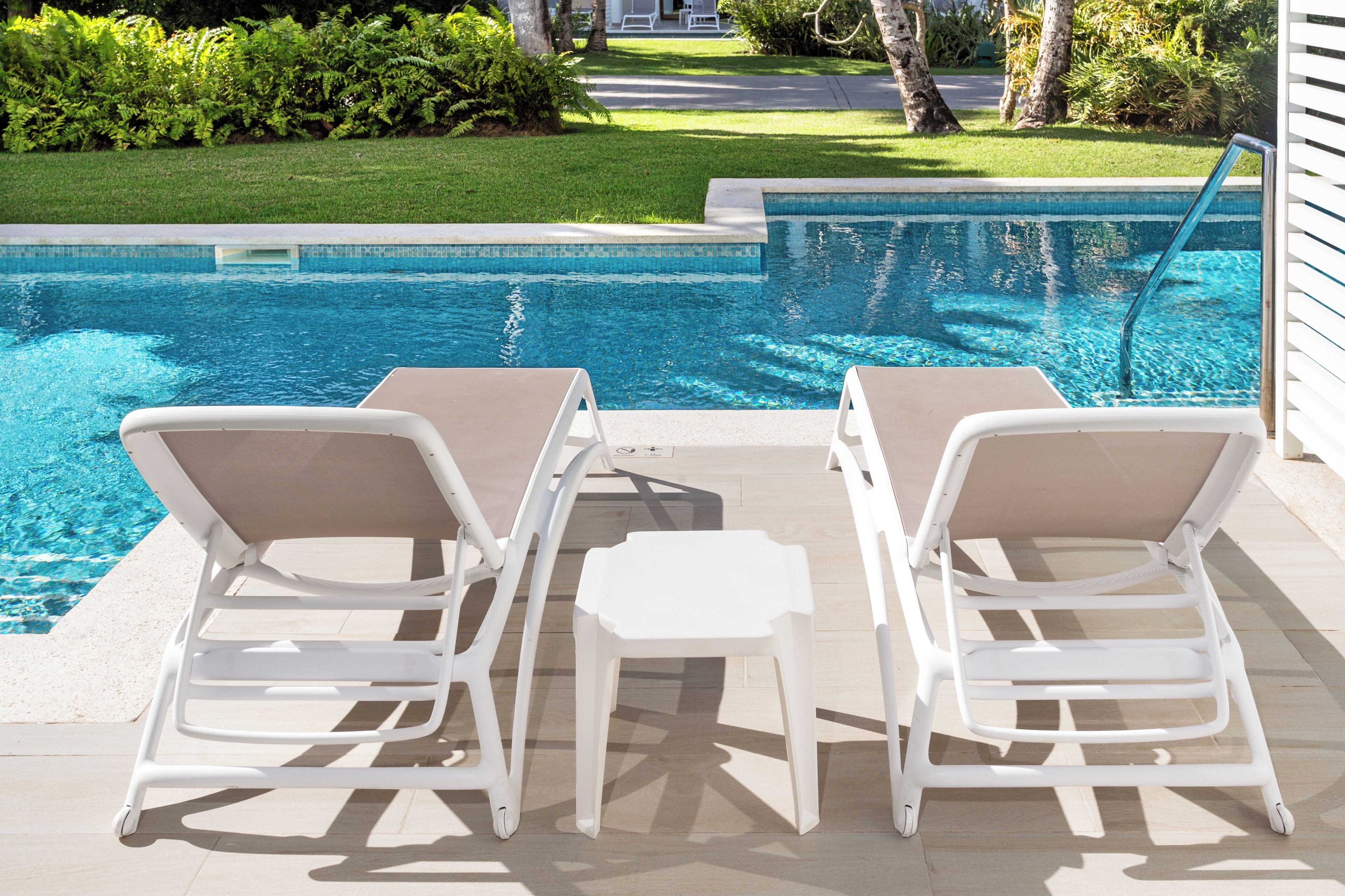 A poolside area with two white lounge chairs and a small table.