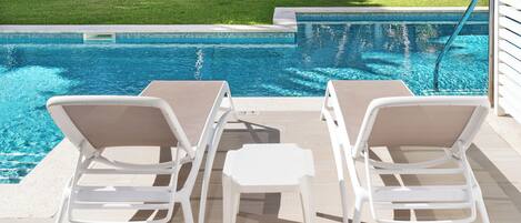 A poolside area with two white lounge chairs and a small table.