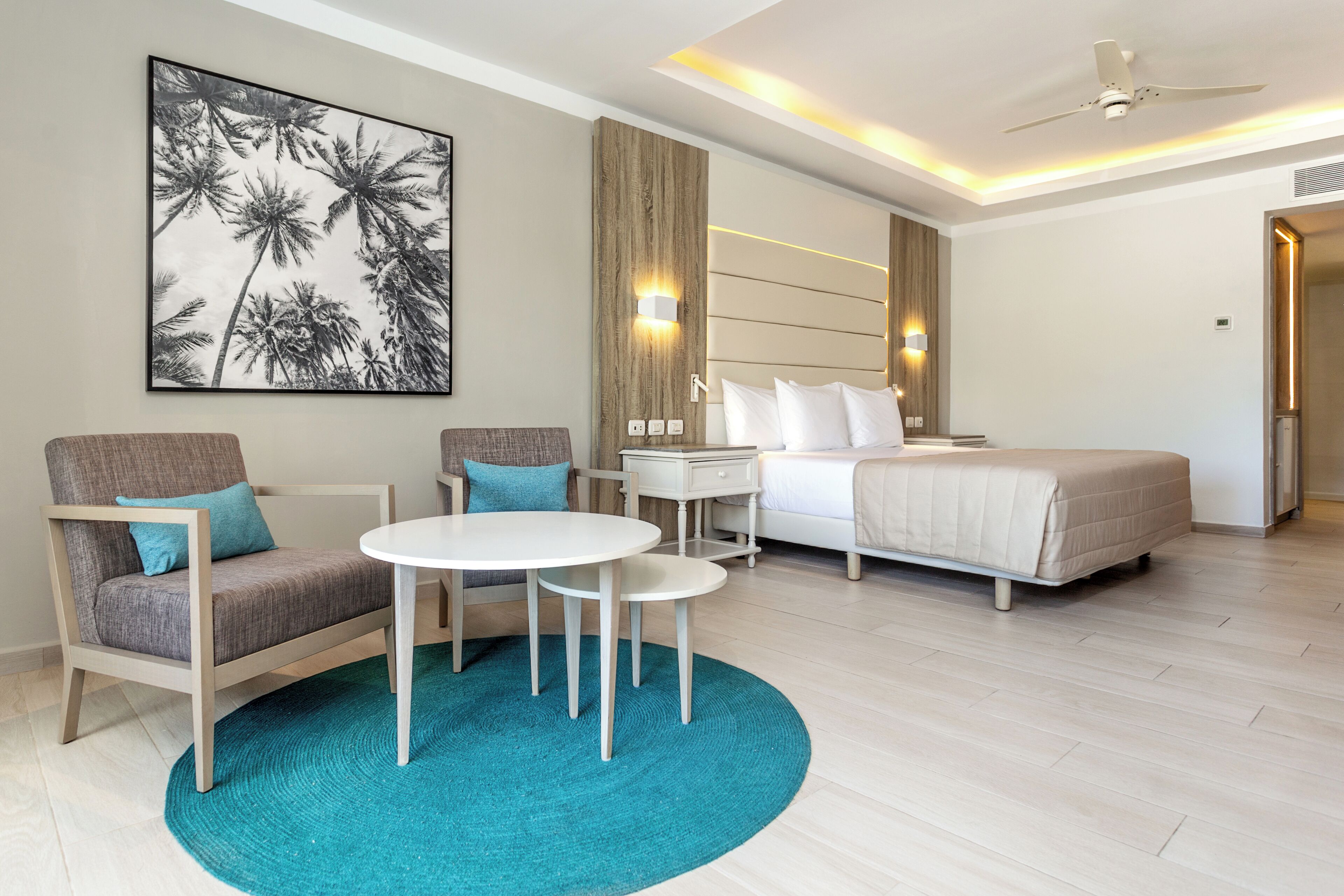 A hotel room with a bed, a desk, a chair, a round table, and a large framed picture on the wall.
