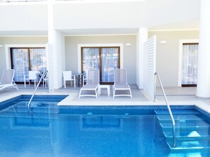 A swimming pool with lounge chairs and a table, surrounded by large windows.