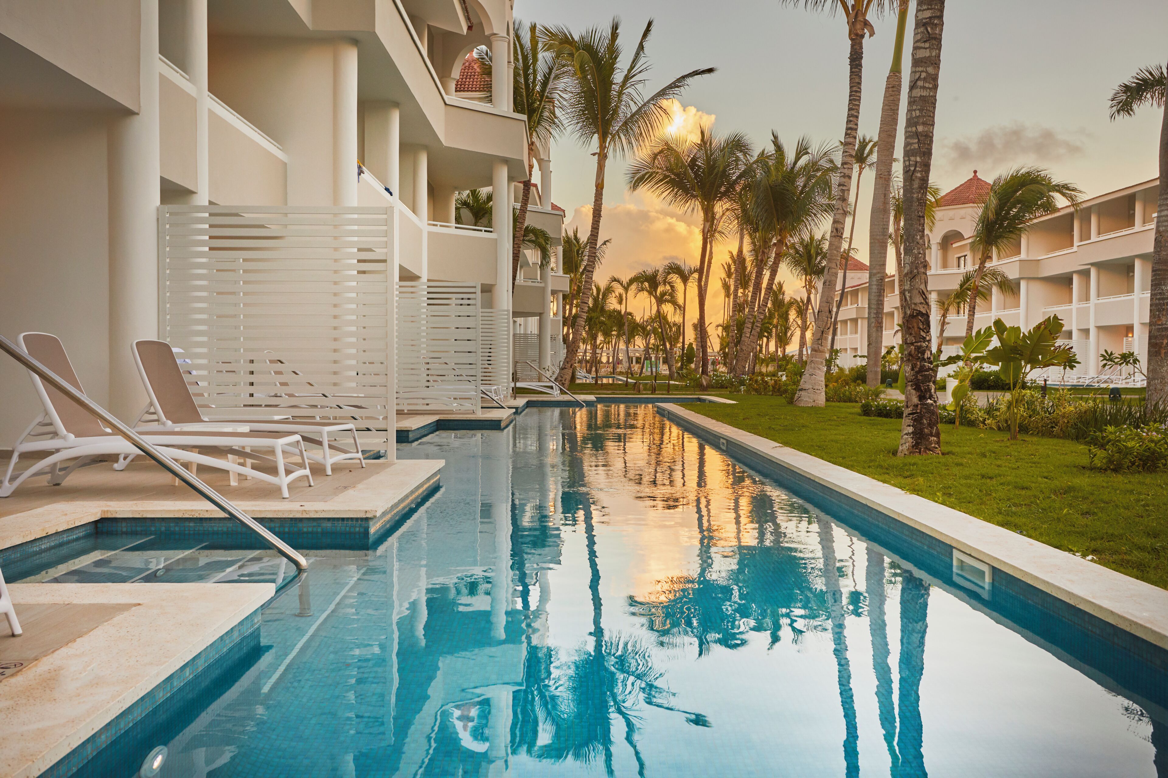 Una piscina con sillas de descanso, palmeras y un edificio con balcones.