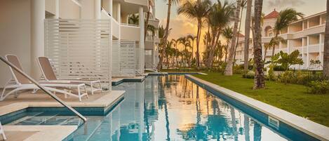 Una piscina con sillas de descanso, palmeras y un edificio con balcones.