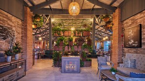 L’intérieur d’un restaurant avec des murs en briques, des plantes suspendues, un grand panneau central portant l’inscription « MEAT », des meubles en bois et un plafond haut avec des poutres apparentes.